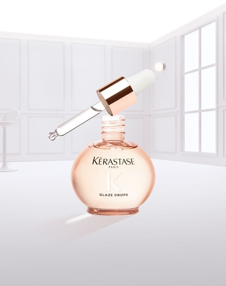 Flacon de gouttes de brillance Kerastase, de couleur rose, avec un compte-gouttes, suspendu et gouttant.