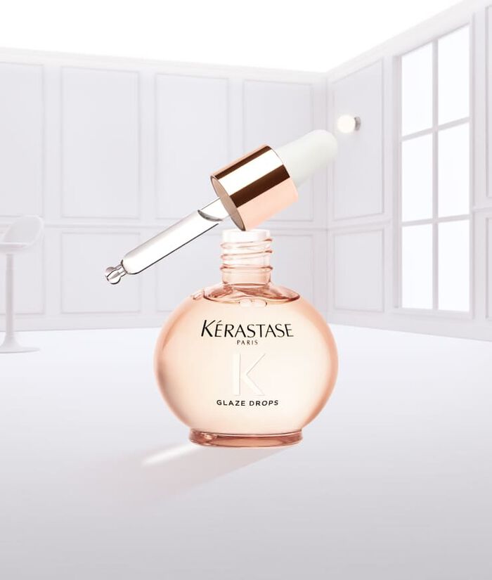 Flacon de gouttes de brillance Kerastase, de couleur rose, avec un compte-gouttes, suspendu et gouttant.