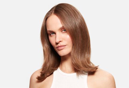 Portrait d'une femme aux cheveux chatains mi-longs, brillants et bien coiffes, sur fond blanc.