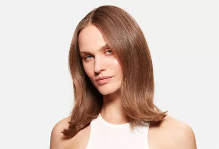 Portrait d'une femme aux cheveux chatains mi-longs, brillants et bien coiffes, sur fond blanc.