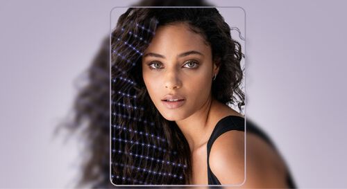 Une femme avec des cheveux boucles, regardant vers l'objectif, avec un fond violet et un eclairage doux.