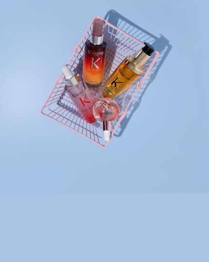 Quatre produits capillaires Kerastase dans des mini-chariots roses sur fond noir : le Serum Nuit 8H Nutritive, l'Huile Originale Elixir Ultime, le Serum Anti-chute Fortifiant de Genesis et les Glaze Drops.