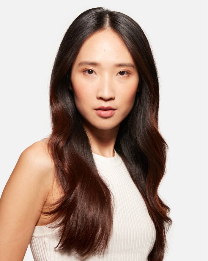 Portrait d'une femme avec des cheveux longs et ondules, portant un haut blanc, affichant une expression serieuse.