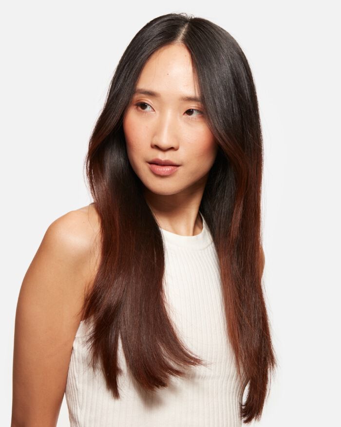 Portrait d'une femme a cheveux longs et lisses, avec une teinte degradee, regardant legerement sur le cote, vetue d'un haut blanc.