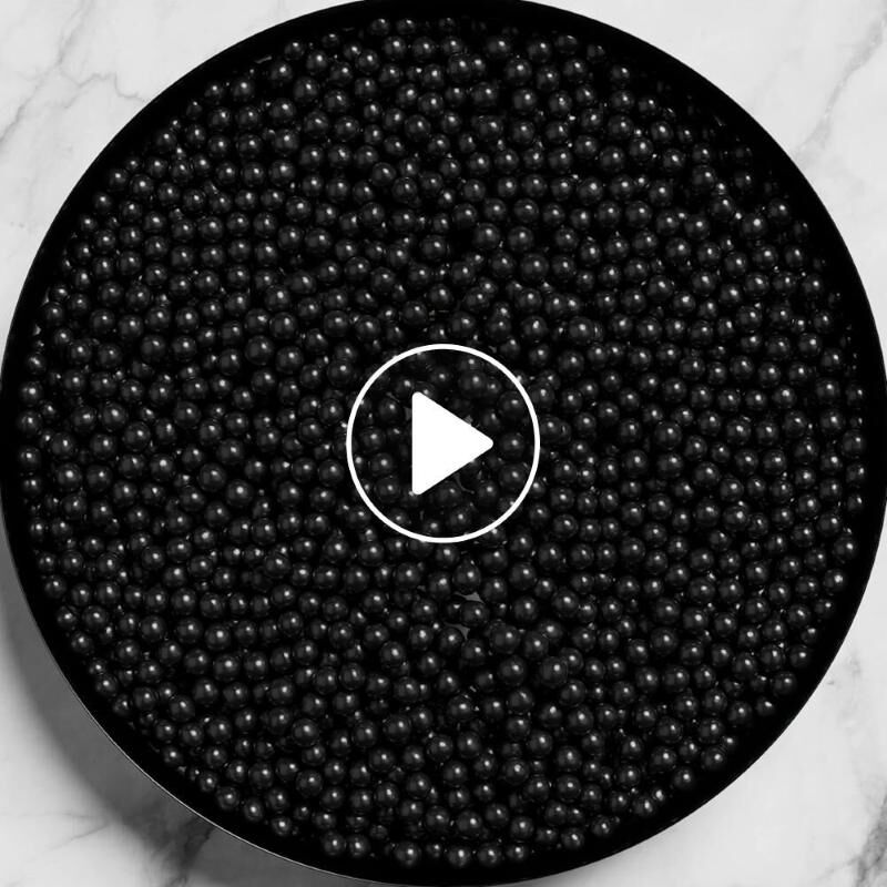 Une vue de dessus d'un recipient circulaire rempli de nombreuses petites perles noires brillantes sur une surface en marbre.