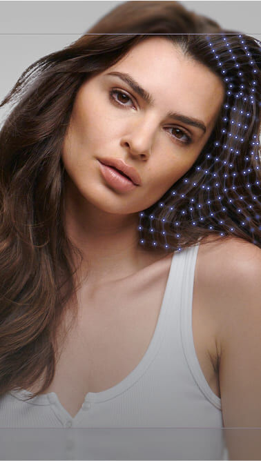 Texte alternatif : Portrait d'une femme avec des cheveux longs et ondules, portant un debardeur blanc, sur fond gris, affichant un leger effet graphique autour de sa tete.