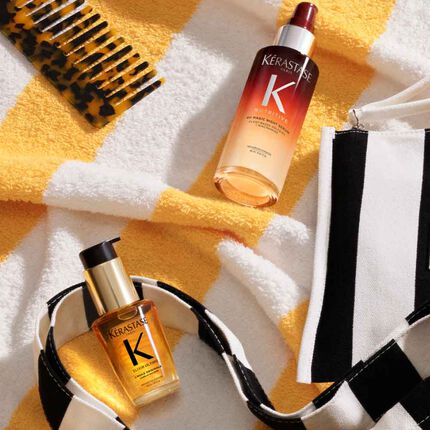 Les produits Kerastase Premiere sont poses sur une serviette de plage jaune rayee, pres de la pochette Kerastase a rayures oranges.