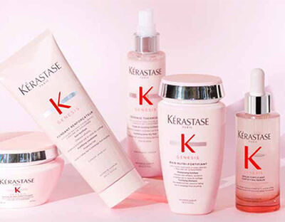 A collection of Kerastase Genesis hair care products displayed on a light pink background, including a shampoo, conditioner, serum, and a restorative mask, all featuring the brand's logo.