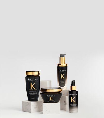 Produits capillaires de la gamme Kerastase Chronologiste dans des flacons noirs et dores, elegamment disposes sur des socles en marbre blanc sur un fond clair.