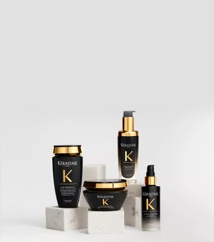 Produits capillaires de la gamme Kerastase Chronologiste dans des flacons noirs et dores, elegamment disposes sur des socles en marbre blanc sur un fond clair.