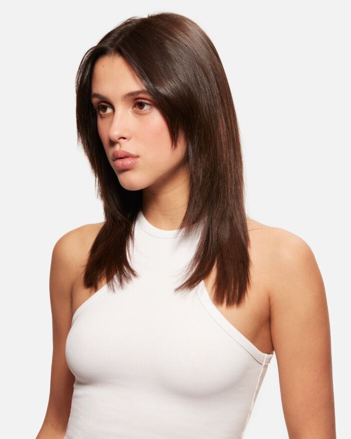 Jeune femme avec des cheveux longs et raides, portant un haut sans manches blanc. Elle a une expression neutre et regarde vers la droite.