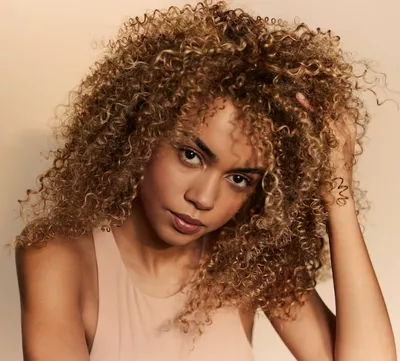 Portrait de femme aux cheveux boucles, volumineux et naturels, illustrant comment integrer un produit anti-humidite dans la routine capillaire