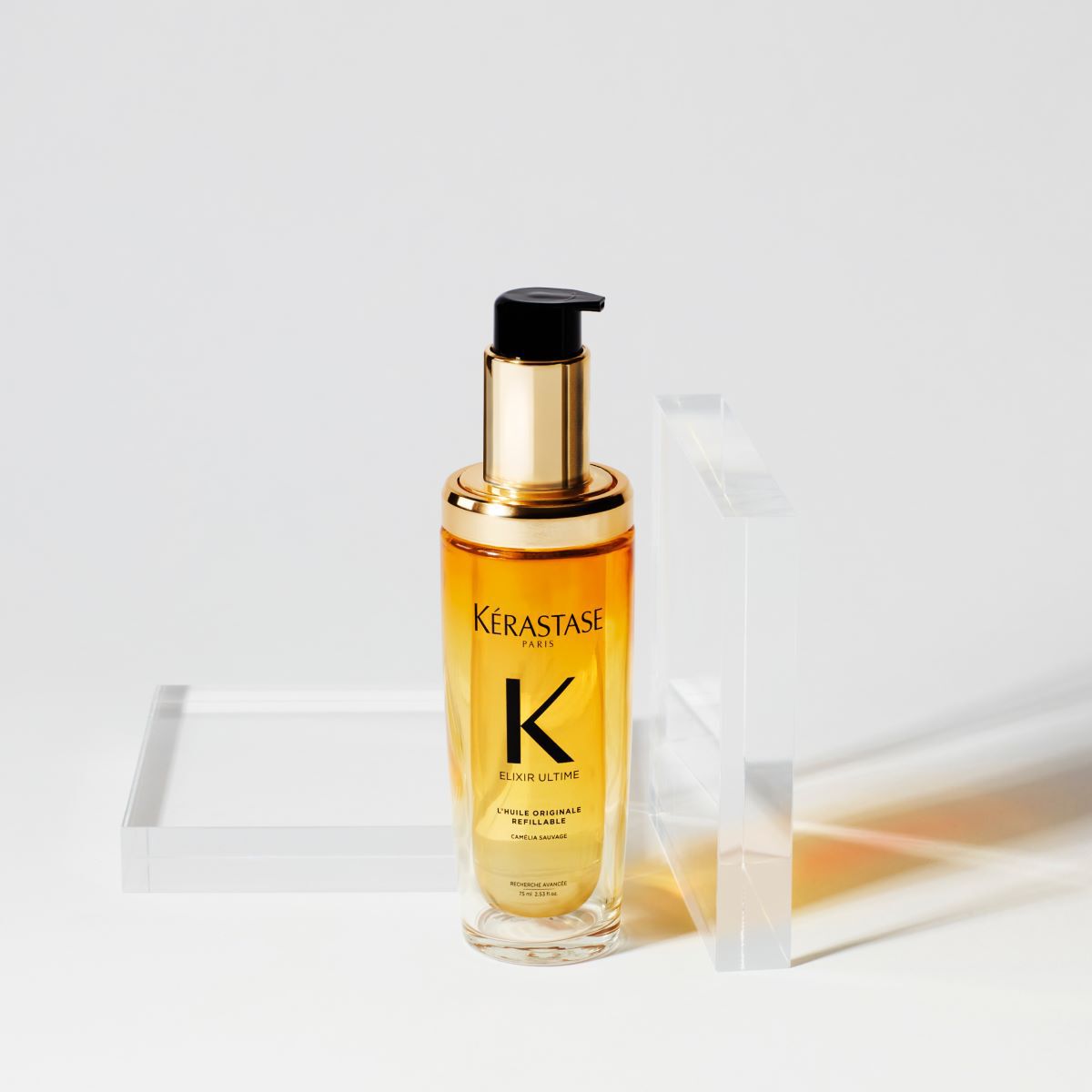 Flacon de serum capillaire Kerastase avec une pompe, pose sur un support transparent, sur fond blanc.