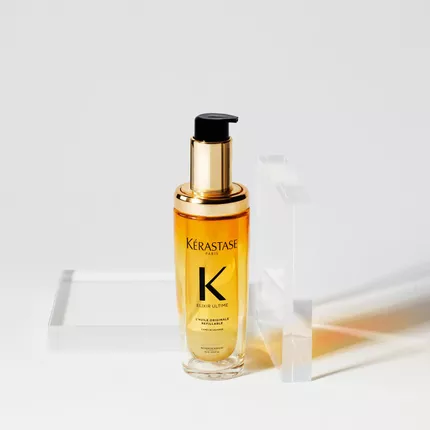 Flacon de serum capillaire Kerastase avec une pompe, pose sur un support transparent, sur fond blanc.