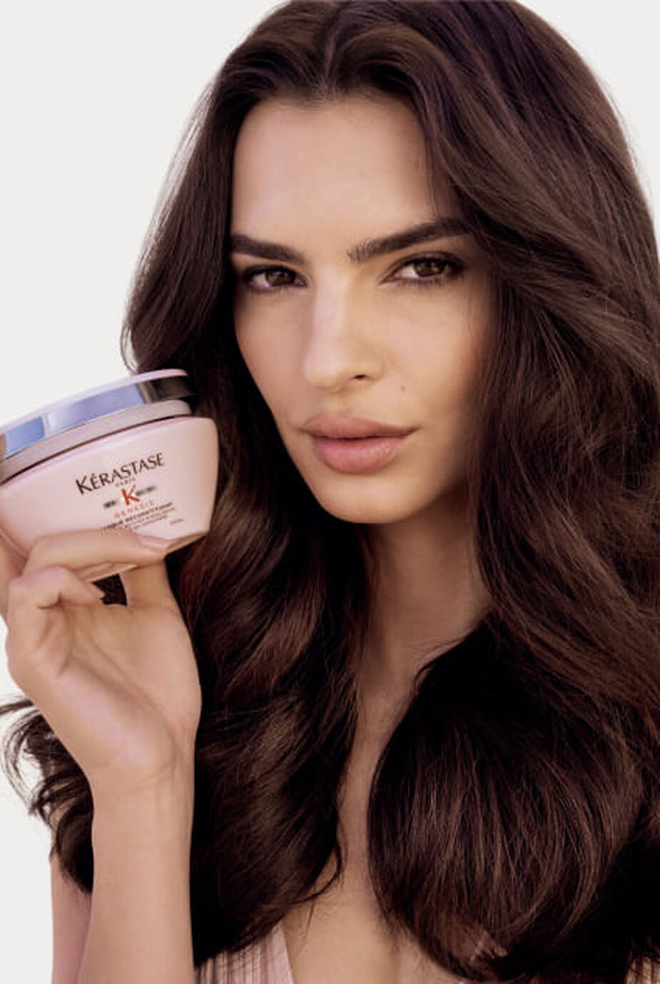 Femme tenant un pot rose de masque Kerastase Genesis Masque Reconstituant, presentant le produit.