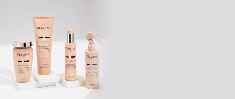 Main tenant un flacon de shampooing Kerastase Gloss Absolu avec un liquide blanc cremeux qui coule dessus.