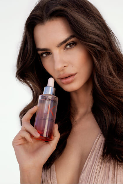 Femme avec un flacon de serum Kerastase Genesis superpose sur sa poitrine, mettant en valeur le produit.