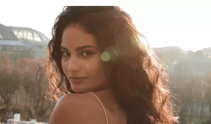 Femme aux cheveux boucles et volumineux eclairee par la lumiere chaude du coucher de soleil, illustrant la routine ideale pour cheveux boucles