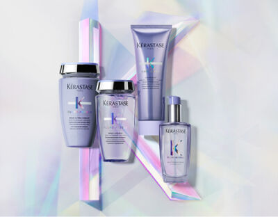 A collection of Kerastase hair care products displayed elegantly on a iridescent background. The products include a shampoo, conditioner, a treatment, and a serum, all presented in sleek packaging with a lavender theme.