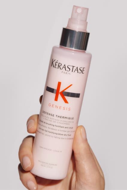 Main tenant un flacon rose de Kerastase Genesis Defense Thermique, un soin protecteur thermique pour cheveux.
