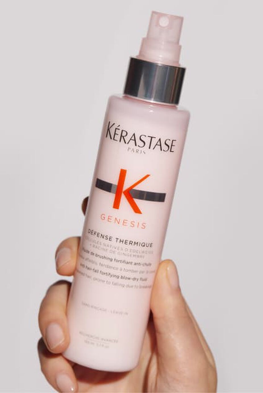 Main tenant un flacon rose de Kerastase Genesis Defense Thermique, un soin protecteur thermique pour cheveux.