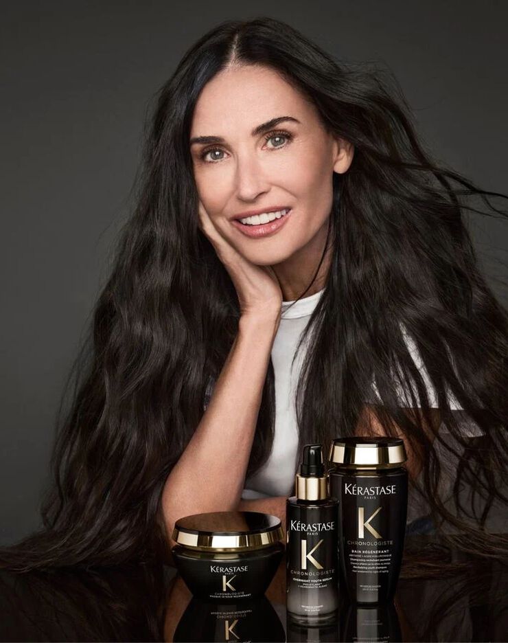 Demi Moore posant avec la gamme de soins capillaires Kerastase Chronologiste aux flacons noirs et dores.