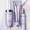 Three Kerastase hair care products are displayed against an iridescent background. The products include a jar, a tube, and a spray bottle, all from the "Blond Absolu" line, featuring a soft purple color scheme.