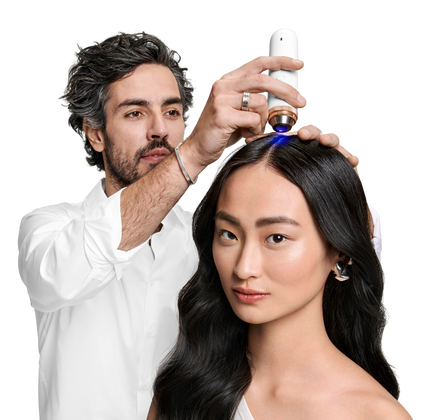 Un homme applique un produit capillaire sur le cuir chevelu d'une femme aux cheveux longs et lisses.