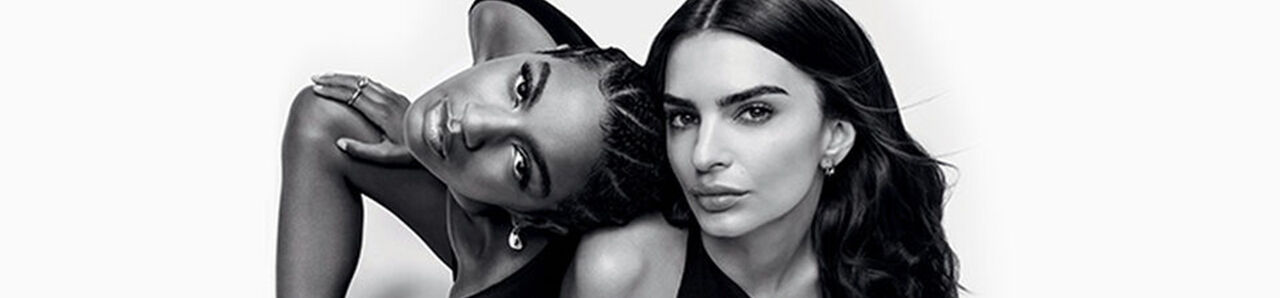 Two models pose together in a black and white photo. One model is leaning back with her head tilted, while the other faces forward, both displaying confident expressions.