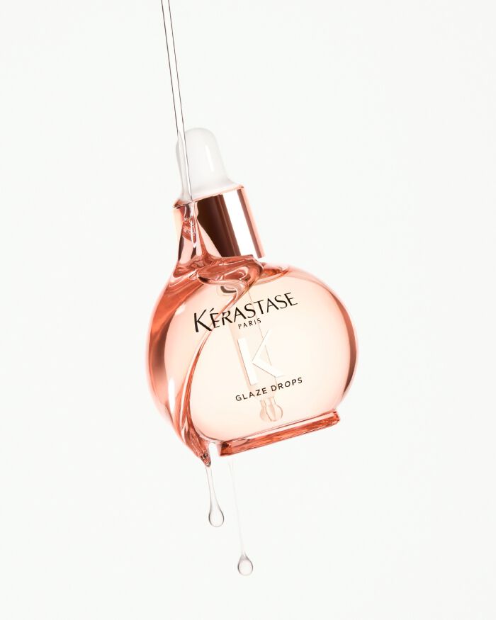 Flacon de gouttes de brillance Kerastase, de couleur rose, avec un compte-gouttes, suspendu et gouttant.