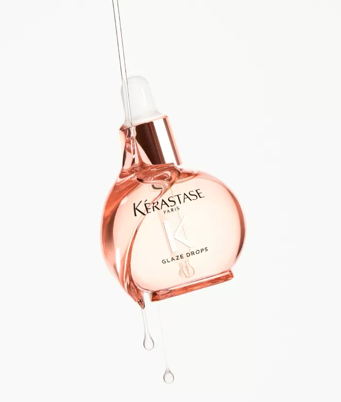 Flacon de gouttes de brillance Kerastase, de couleur rose, avec un compte-gouttes, suspendu et gouttant.