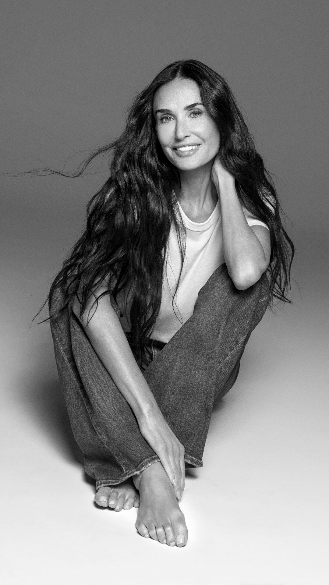 Demi Moore assise en tailleur avec un grand sourire eclatant.
