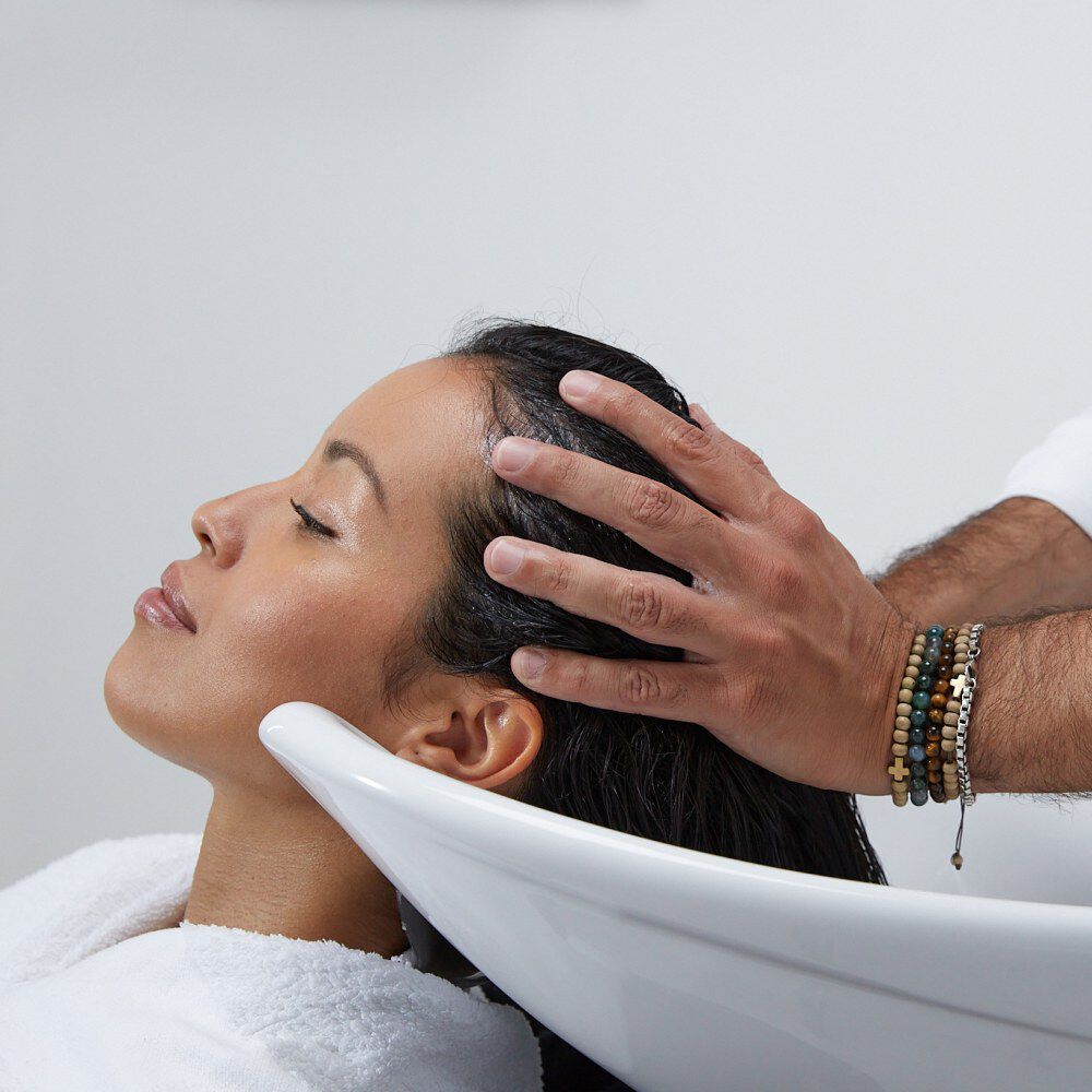 Une femme recoit un massage du cuir chevelu pendant un shampooing dans un salon de coiffure.