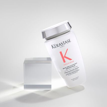 Bouteille de shampooing Kerastase "K Premiere" inclinee sur un fond neutre, avec un cube transparent a cote.