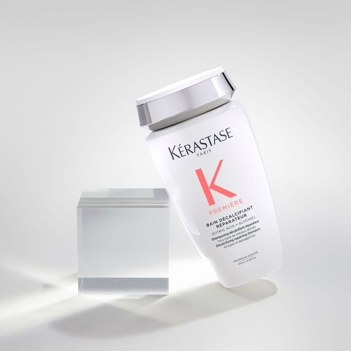 Bouteille de shampooing Kerastase "K Premiere" inclinee sur un fond neutre, avec un cube transparent a cote.