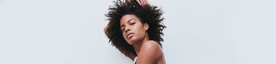 A person with curly hair poses against a light background, showcasing a confident expression.