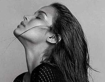 A close-up of a woman with long, wet hair cascading down her back, her head tilted slightly back, and her profile elegantly highlighted against a neutral background.