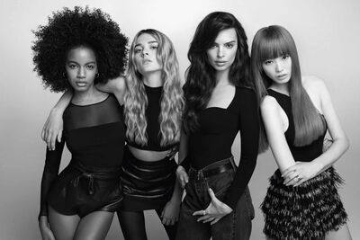 A group of four diverse women poses together in a stylish black and white photograph. They have various hairstyles and outfits, exuding confidence and elegance.