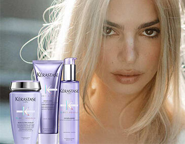 A model with long, light blonde hair is featured prominently alongside Kerastase hair care products displayed in the foreground, including shampoo, conditioner, and a treatment. The background has a soft, blurred effect, creating a focus on the model and the products.