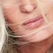 Close-up of a woman's face with blonde hair blowing across her lips, highlighting soft skin and natural beauty.
