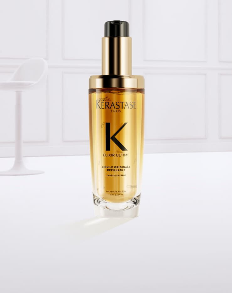 Flacon de serum Kerastase Elixir Ultime, entoure de gouttes d'huile doree sur fond clair.