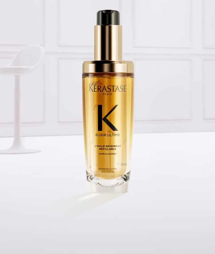 Flacon de serum Kerastase Elixir Ultime, entoure de gouttes d'huile doree sur fond clair.