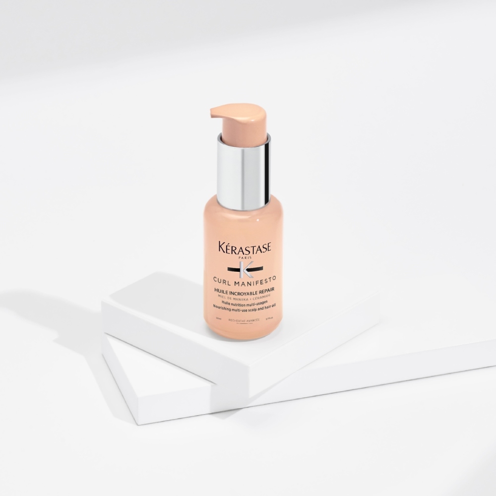 L'huile capillaire Curl Manifesto Huile Sublime Repair est présentée sur un fond gris pur avec des cubes transparents. Cette huile hydrate et définit la forme des cheveux bouclés tout en réduisant les frisottis et la casse.