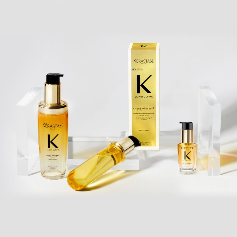 La nouvelle huile capillaire Elixir Ultime, sa recharge et le format voyage sont présentés sur des cubes transparents sur fond gris pur.