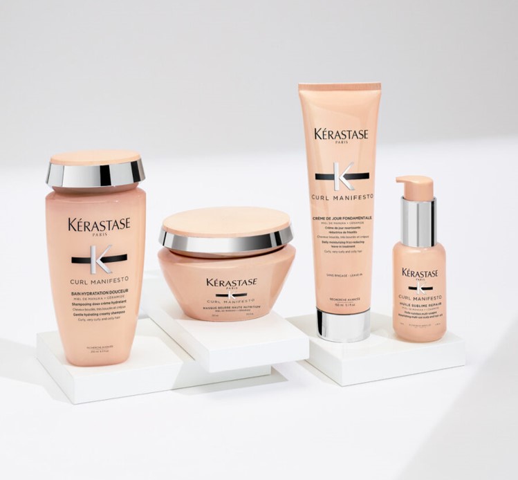 Quatre produits de soins capillaires Kérastase de la gamme Curl Manifesto sur un socle blanc, avec un fond neutre.