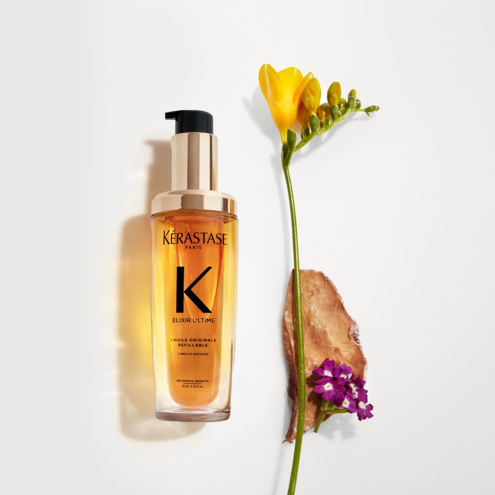 Le nouvel Elixir Ultime rechargeable est présenté sur un fond gris pur avec des fleurs de freesia et d'héliotrope, et du bois de santal.