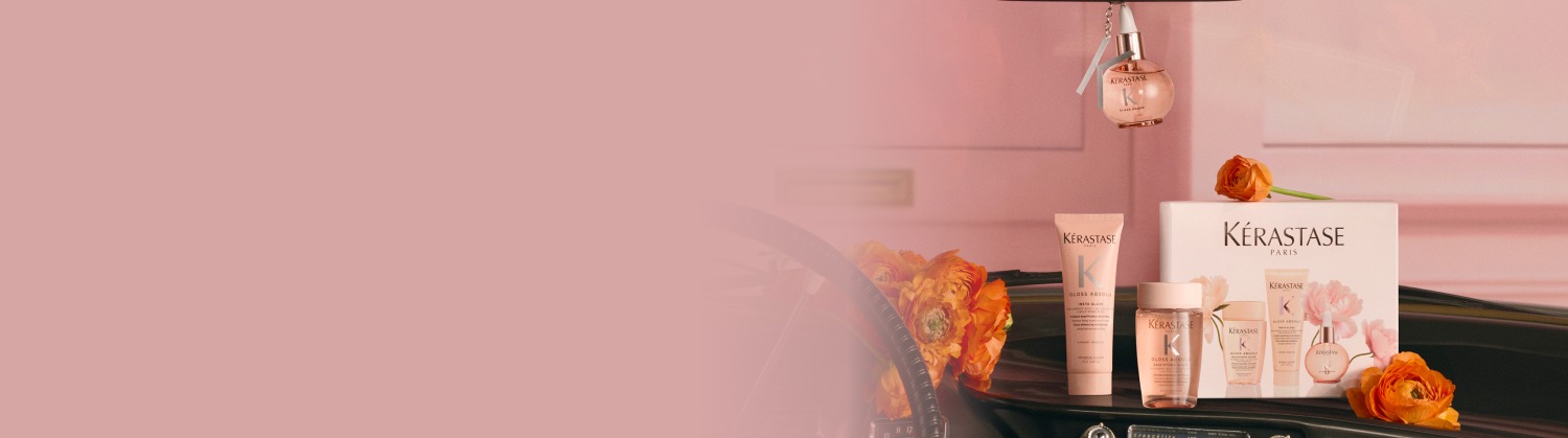 Image de produits capillaires Kerastase disposés pour un cadeau, incluant plusieurs flacons dorés, une bougie parfumée et une pochette blanche en tissu éponge, le tout présenté dans un emballage festif blanc et doré sur un fond blanc et lumineux. L'ensemble évoque le luxe et l'élégance.