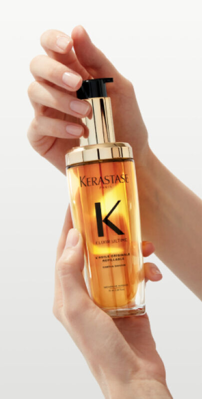 Flacon de sérum capillaire Kerastase Elixir Ultime, tenu entre deux mains délicates, sur fond neutre.